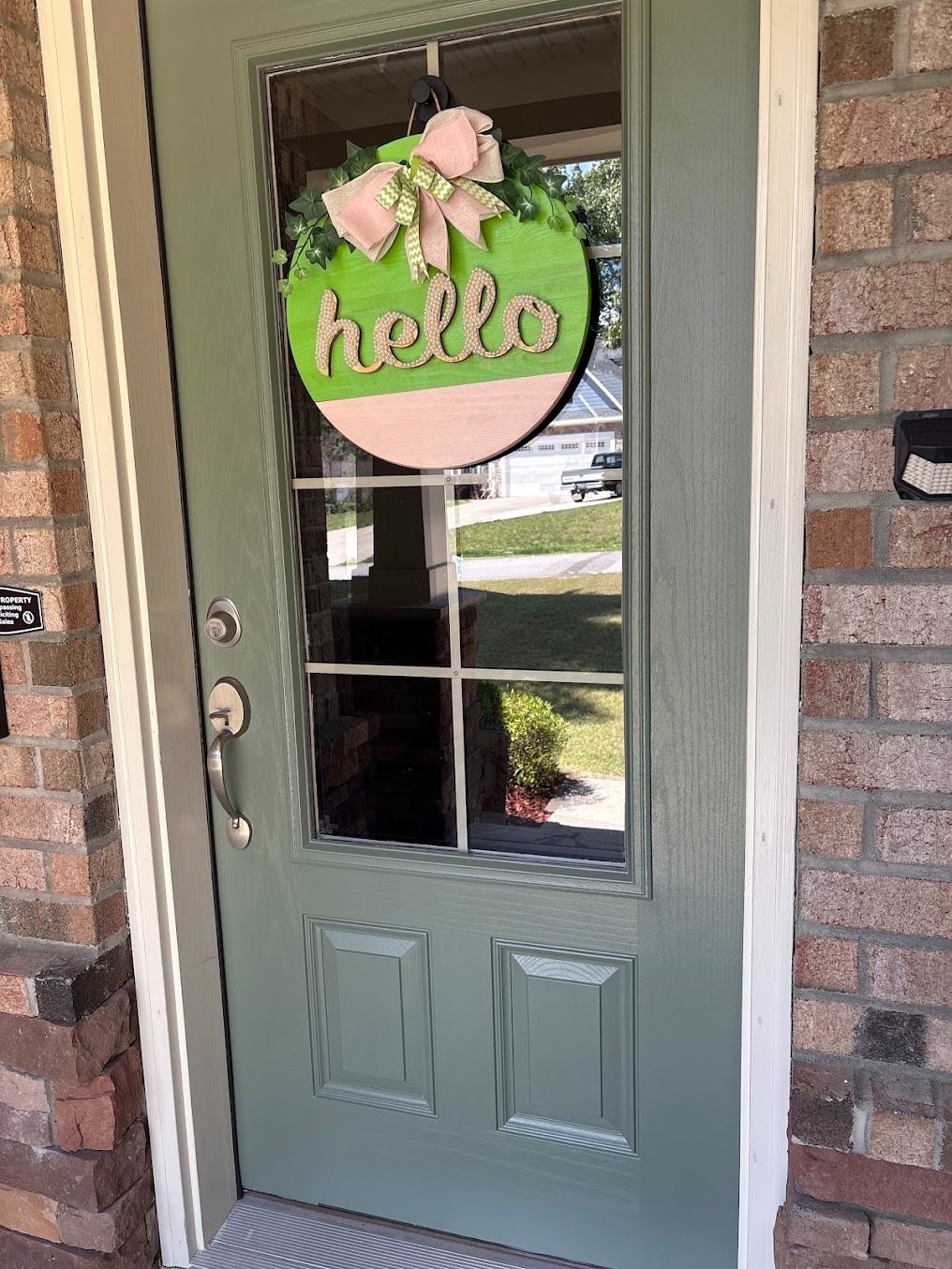 Green front door with a pink-and-green “hello” wreath on a brick porch