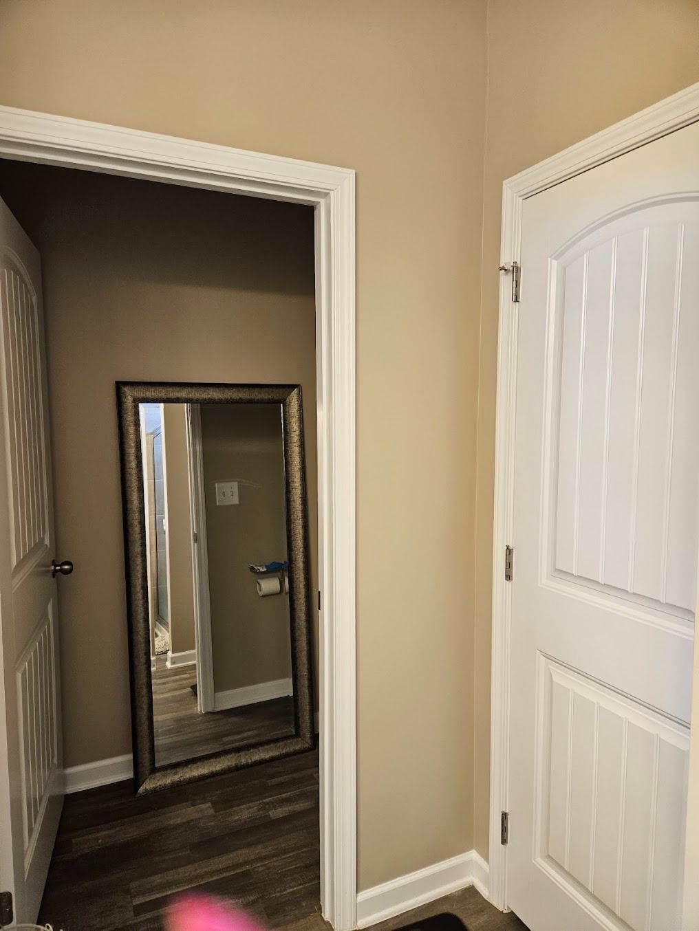 Interior hallway with beige walls, white doors, and a floor mirror leaning in a doorway.