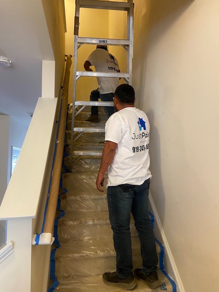 Two workers moving a wrapped object up a narrow stairwell in a hallway.