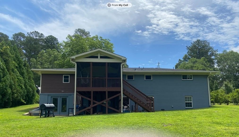 Green house with a covered porch and stairway, set in a grassy yard under a blue sky.