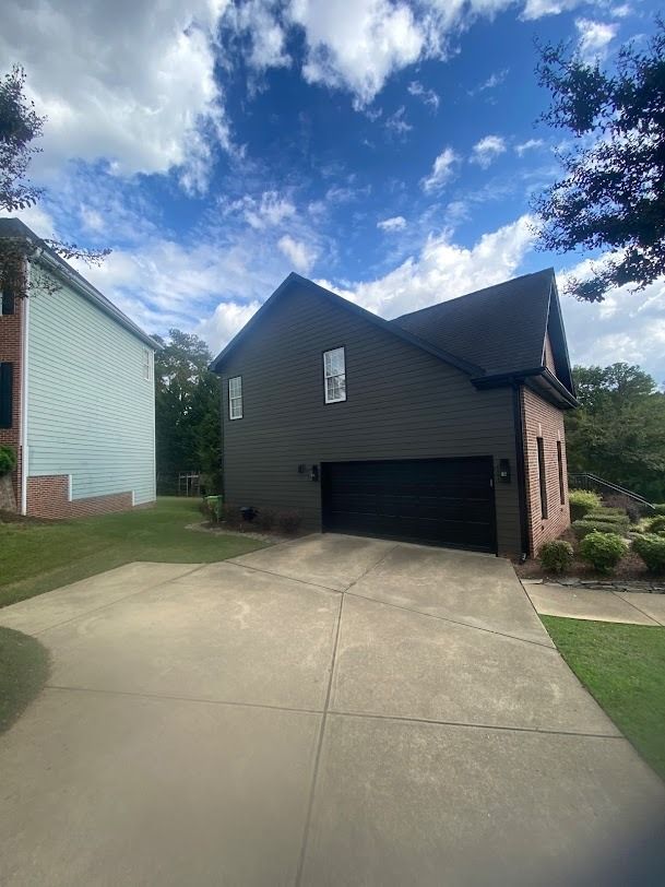 Suburban house with a dark exterior, two-car garage, and concrete driveway under a blue sky
