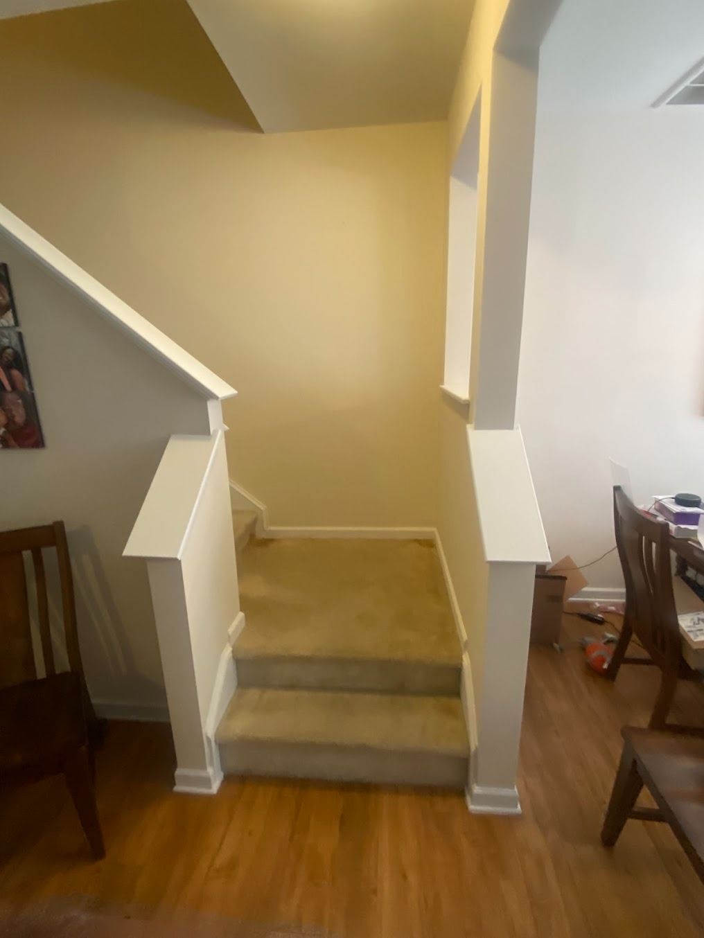 Short carpeted stairway between rooms with beige walls and white trim, beside wood floors and chairs