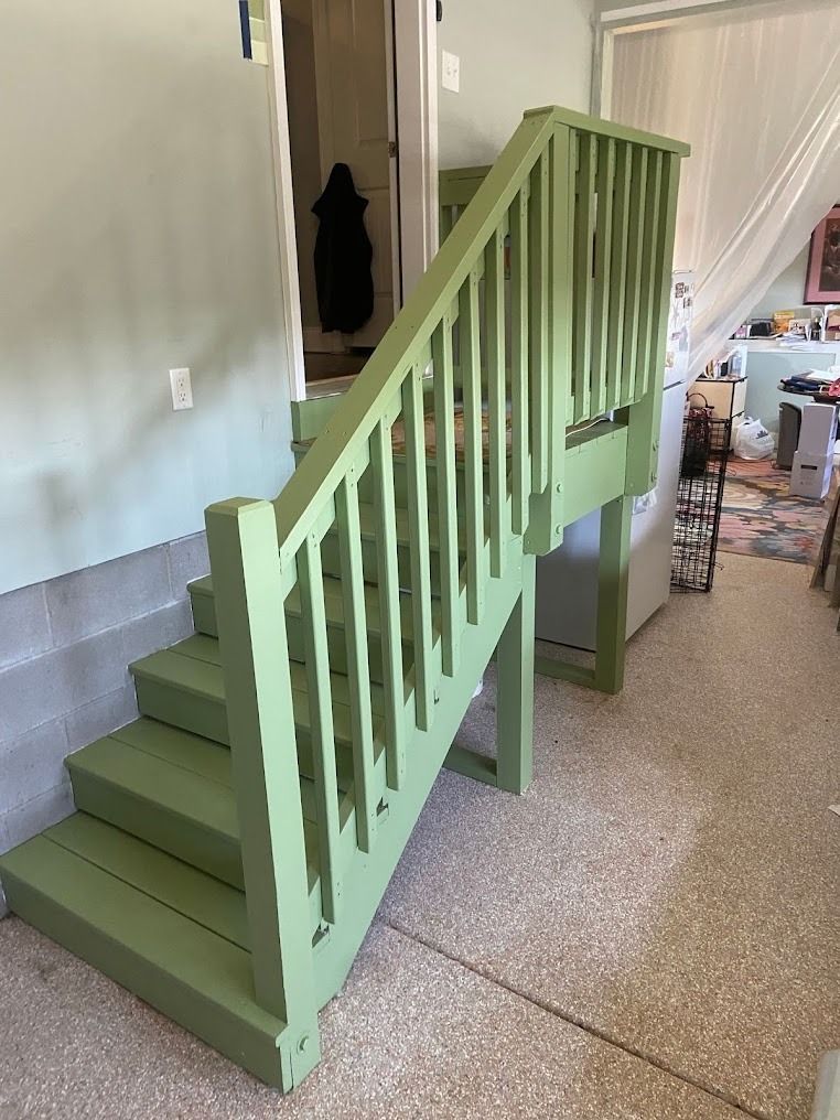Mint-green staircase with railings inside a home, shown on a carpeted floor beside a doorway.