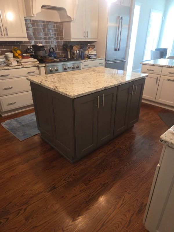 Kitchen with dark wood island, granite countertop, stainless stove, white cabinets, and hardwood floor.