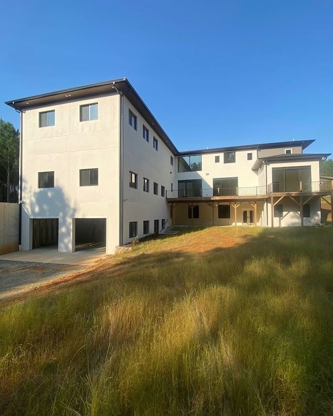 Modern beige apartment building with large windows and grassy yard under a clear blue sky