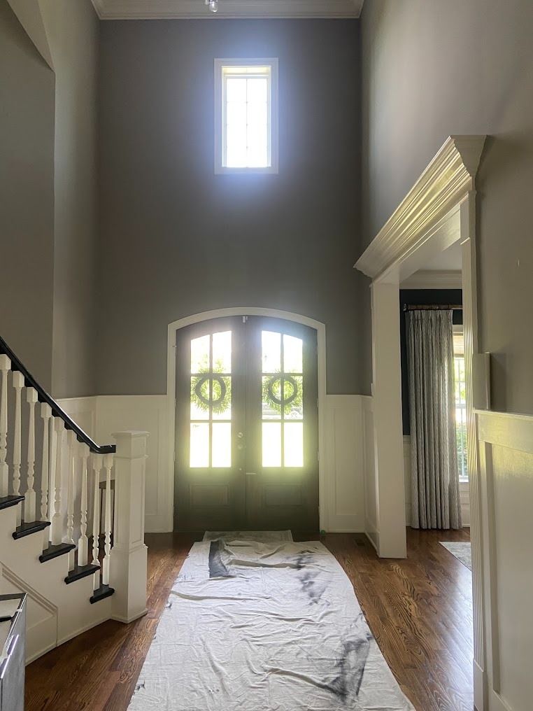 Front entry hallway with tall arched window, white staircase, and a drop cloth on the hardwood floor