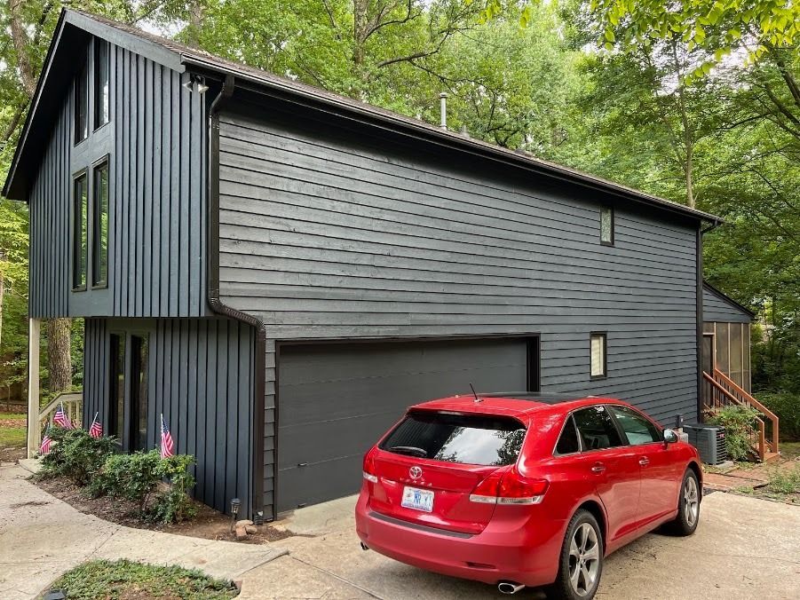 Modern dark-gray house with a red car parked in front, surrounded by trees