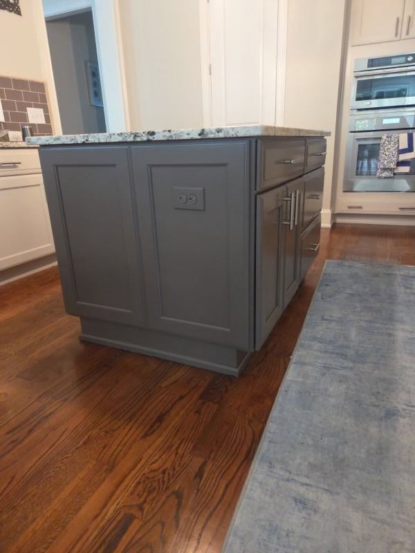 Gray kitchen island with a dark stone countertop in a bright hardwood-floored kitchen
