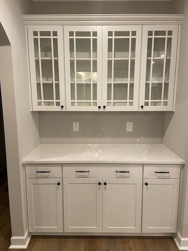 White built-in kitchen cabinets with glass-front uppers and a light countertop in a small alcove