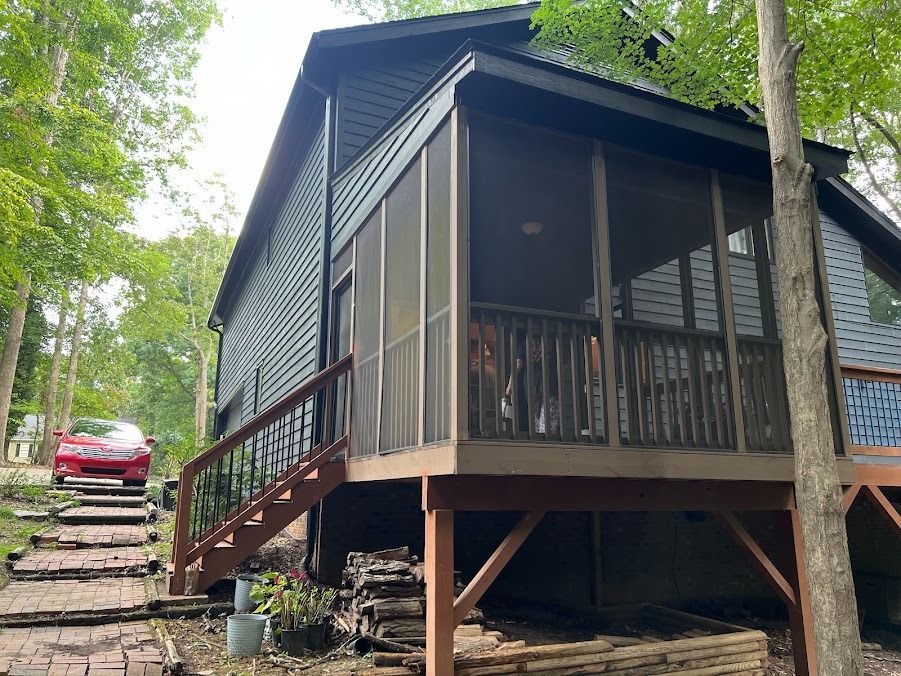 Wooden cabin on a wooded hillside with a red truck parked beside steps leading up the slope