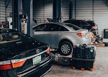 Cars in a mechanic's shop; silver car on a lift, other cars are black.