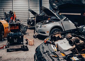 Cars with open hoods in an auto repair shop. Mechanics are likely working on them.