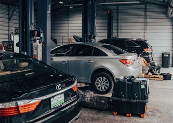 Cars in a car repair shop. Silver car on a lift. Tools and equipment scattered about the garage.