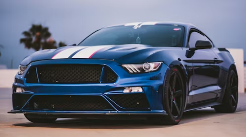 Blue sports car with black hood and grille parked outdoors at sunset