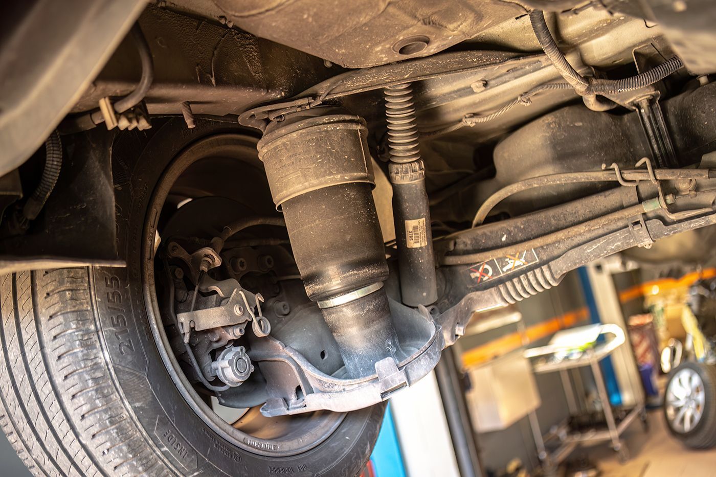 Underside view of a car's rear suspension, highlighting an air spring and shock absorber near a tire.