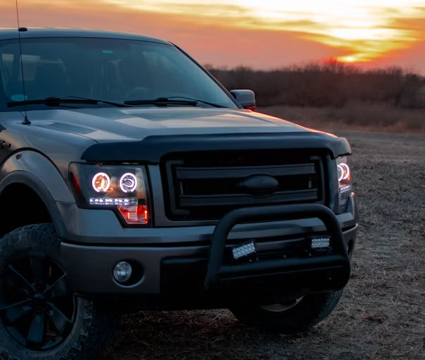 Black pickup truck parked at sunset on a dirt road with headlights on