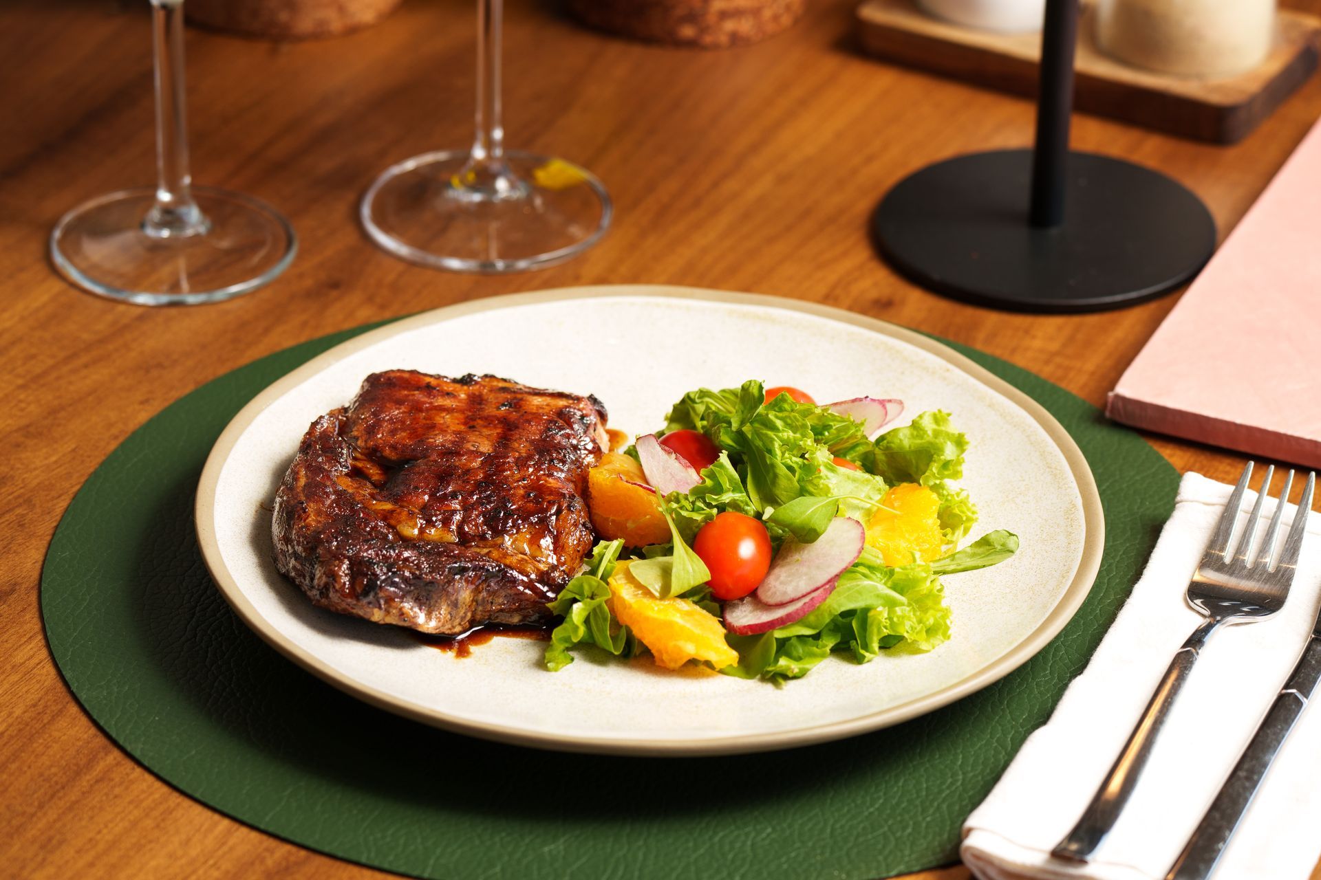 Filete con ensalada mixta en un plato blanco en una mesa de restaurante con copas de vino y cubiertos.