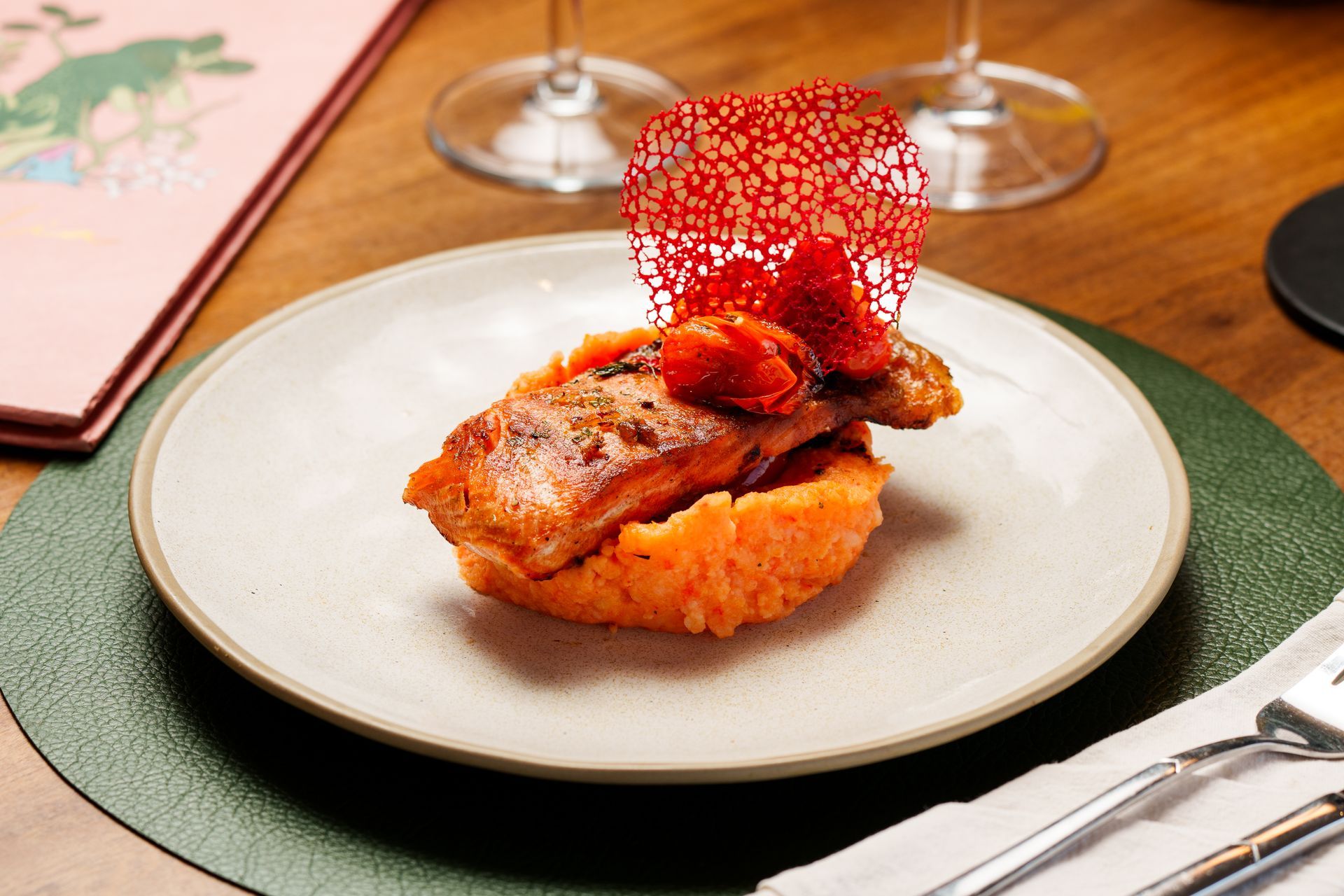 Plato gourmet de pescado con puré de naranja y guarnición crujiente roja sobre un plato blanco.