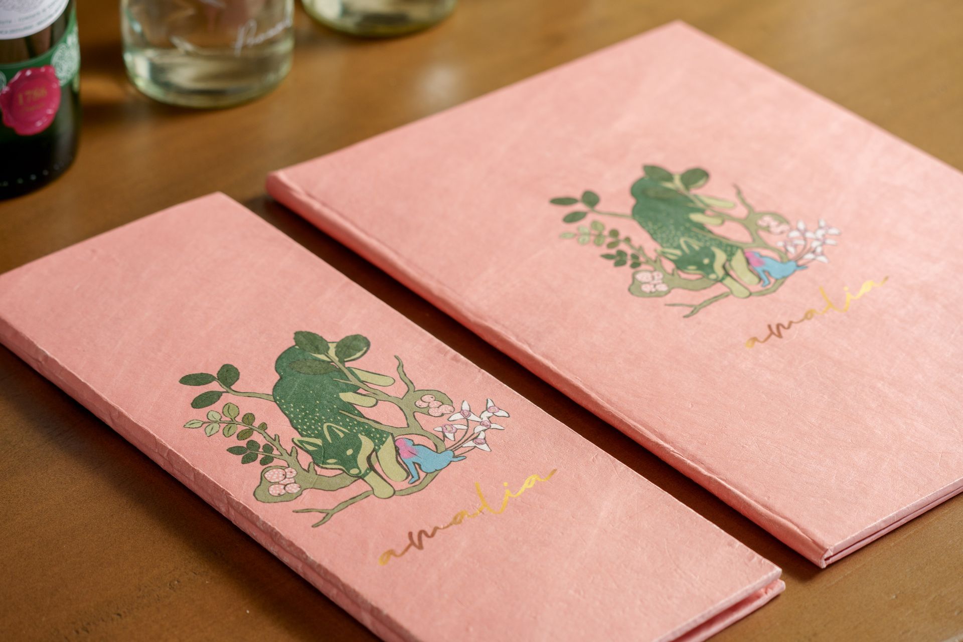 Dos cuadernos rosas con ilustraciones florales sobre una mesa de madera.