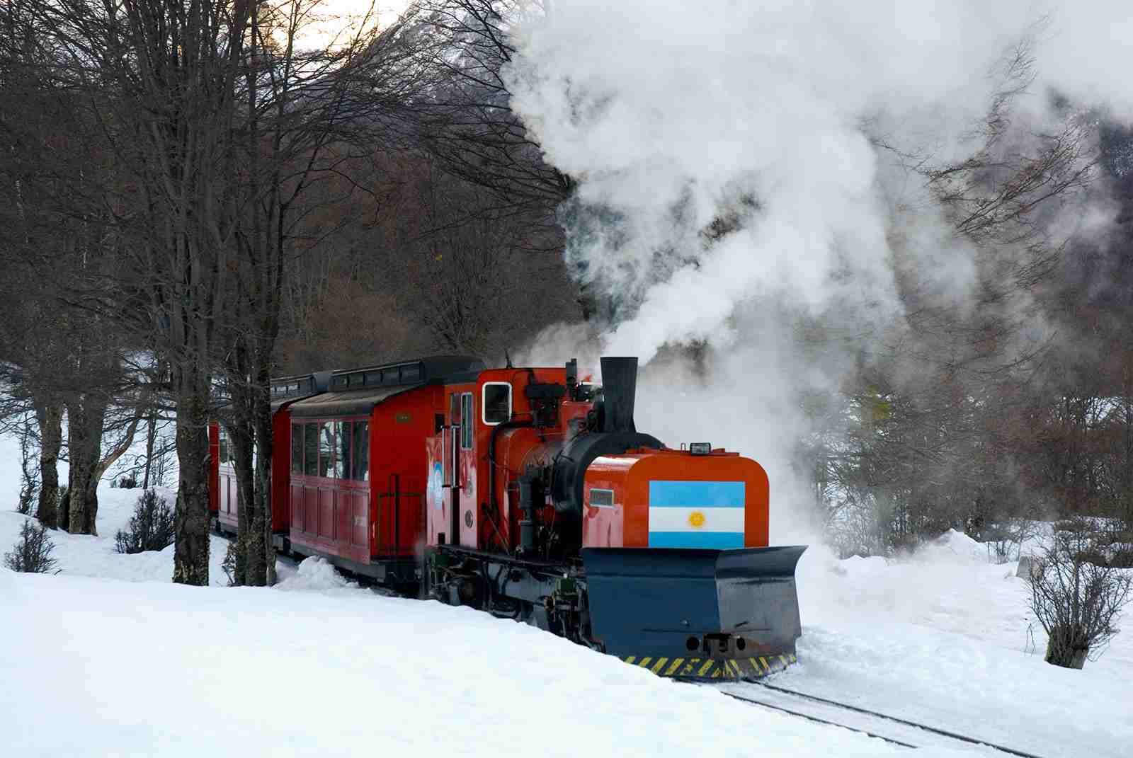 Tren rojo con motor de vapor viajando a través de bosques nevados.