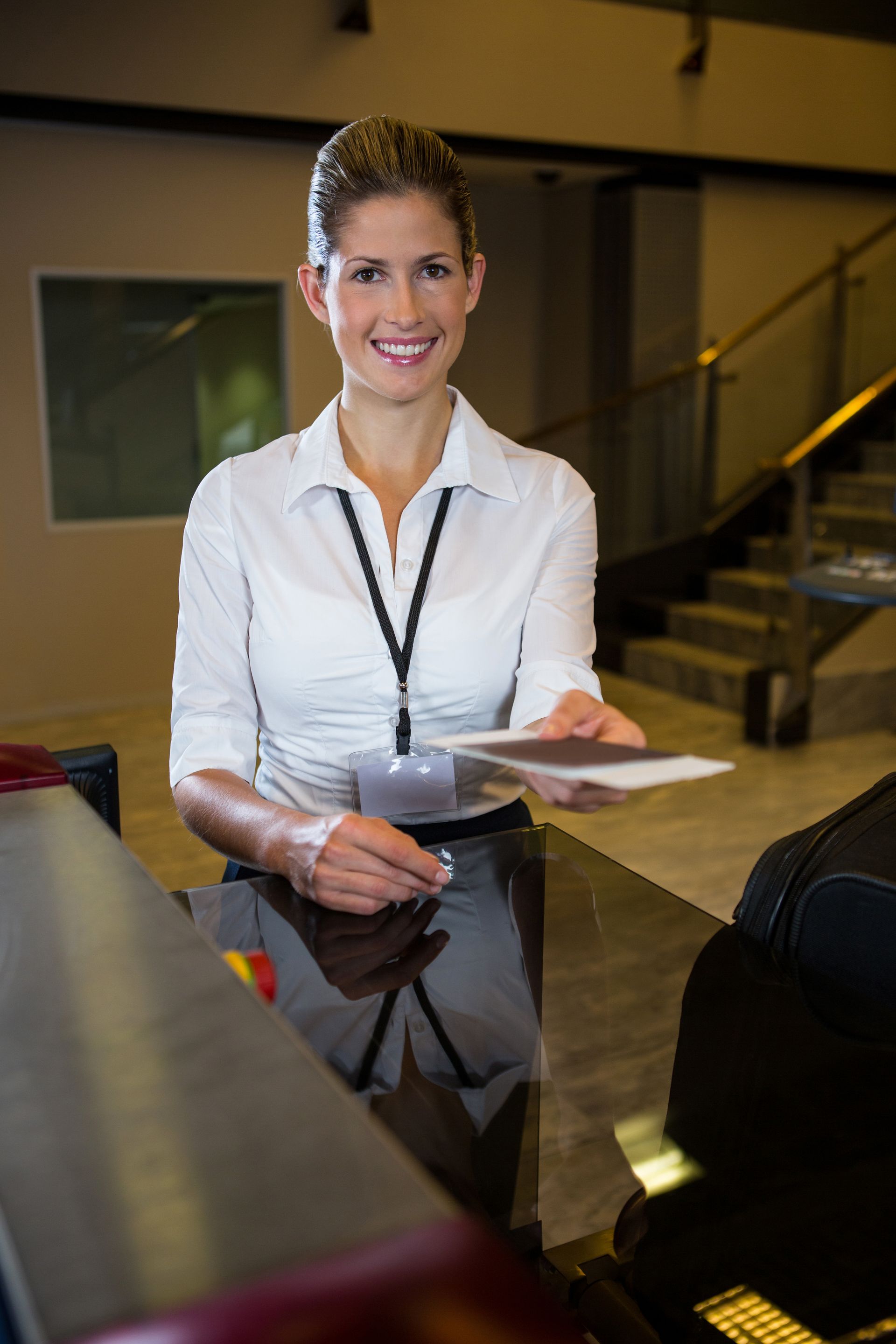 Recepcionista sonriente con blusa blanca sosteniendo una tarjeta en la recepción de un hotel.