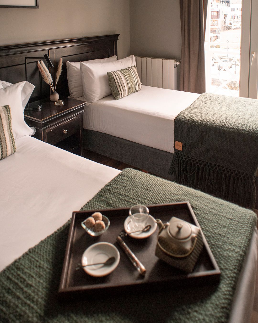 Dos camas individuales perfectamente hechas en una habitación de hotel, con una bandeja de té sobre la cama que está en primer plano.