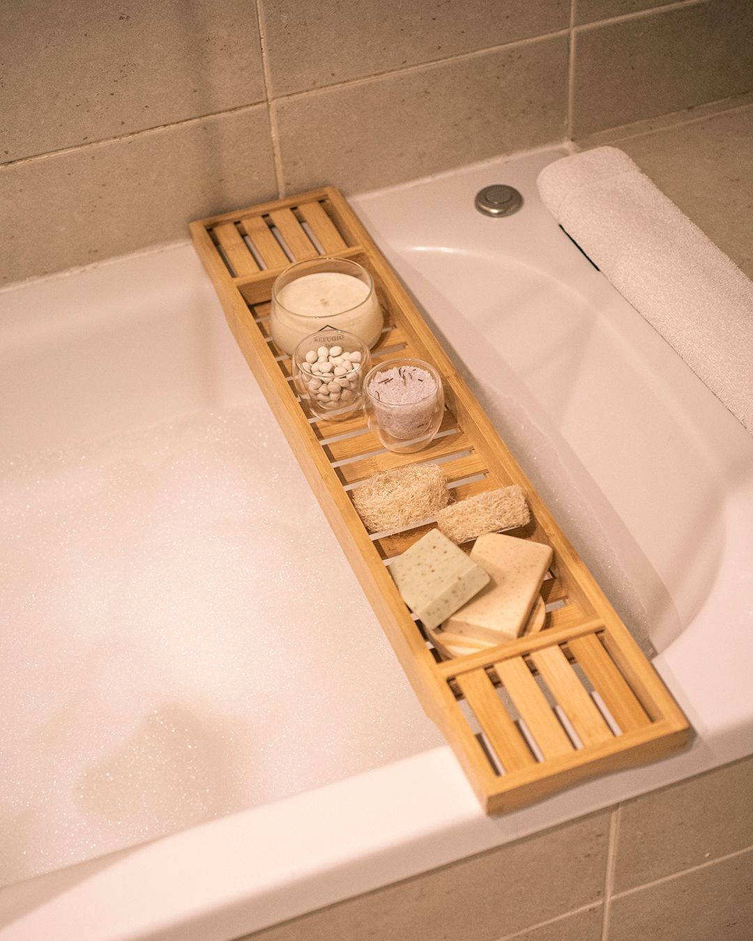 Bandeja para bañera con velas, jabón y accesorios de baño junto a burbujas.