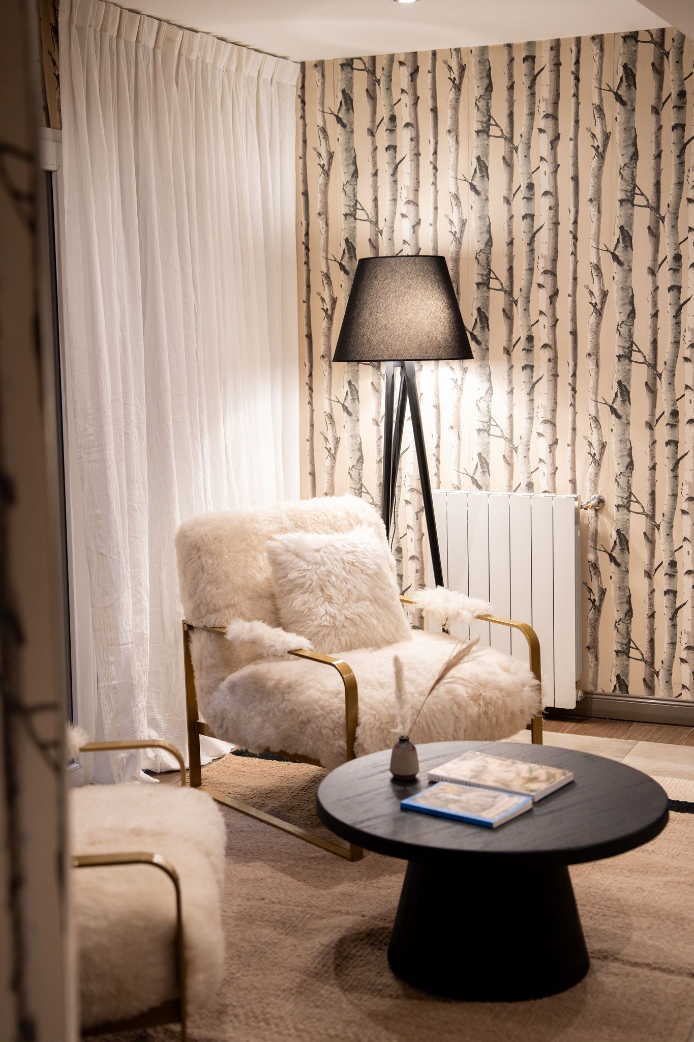 Acogedora sala de estar con sillón mullido, lámpara de pie negra, mesa de centro redonda y papel tapiz floral.