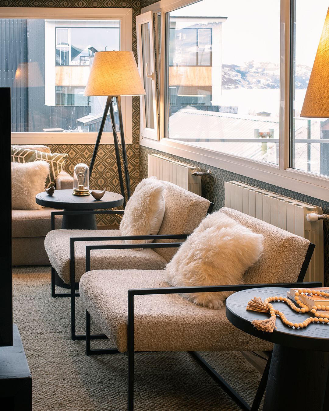 Acogedor salón moderno con sillones de piel, lámpara de pie, mesas auxiliares y vistas a la ciudad nevada a través de grandes ventanales.