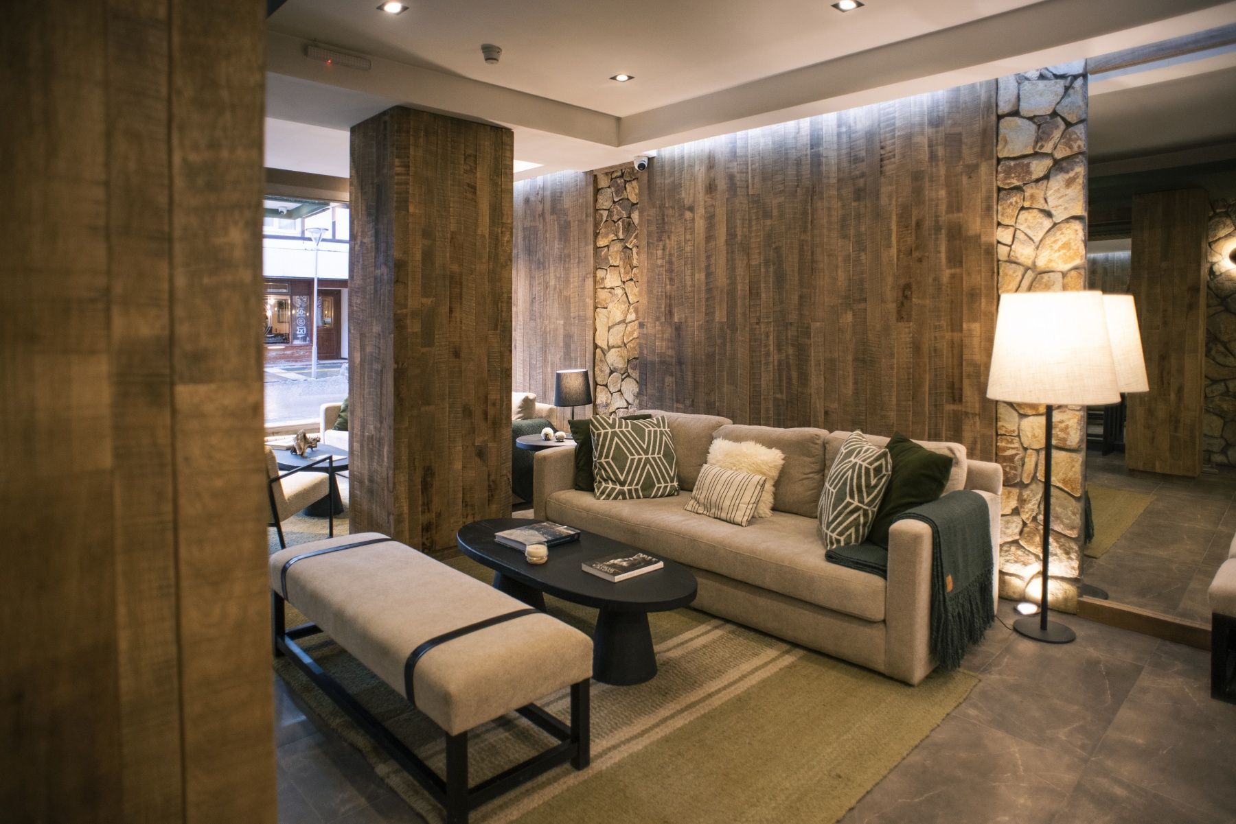 Sala de estar moderna con sofá beige, banco, lámpara de pie y paredes revestidas de madera.