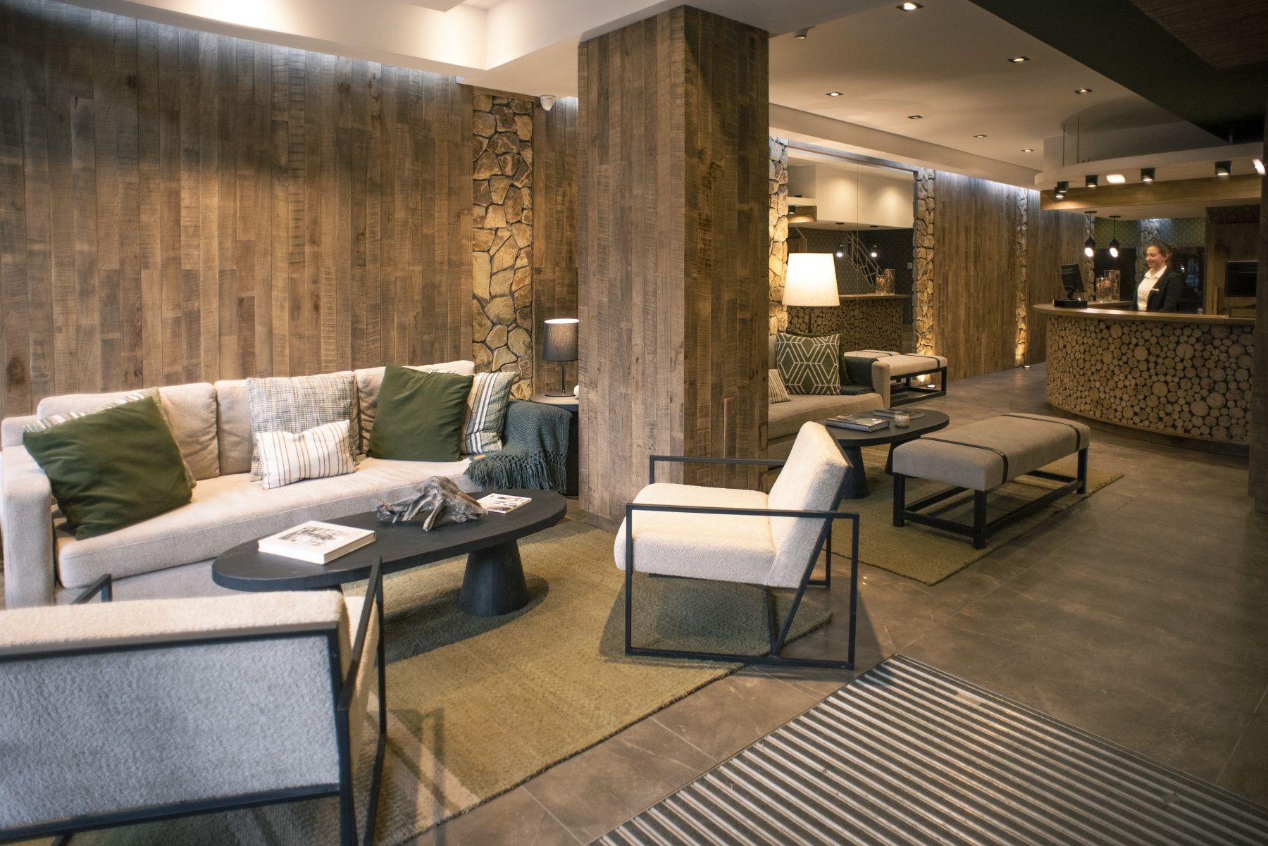 Salón moderno con sofás grises, paredes revestidas de madera, mesas de centro e iluminación ambiental cálida.