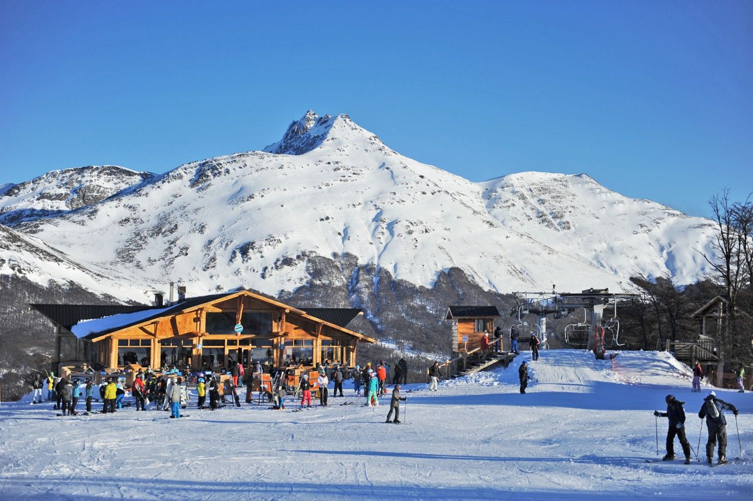 Refugio de esquí en la base nevada de la montaña con esquiadores en un día soleado de invierno.