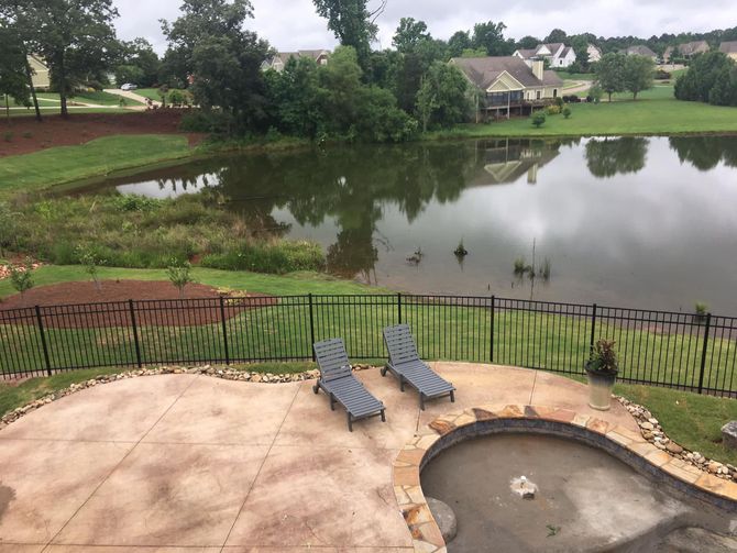 Patio with loungers and hot tub overlooking a calm pond and fenced yard