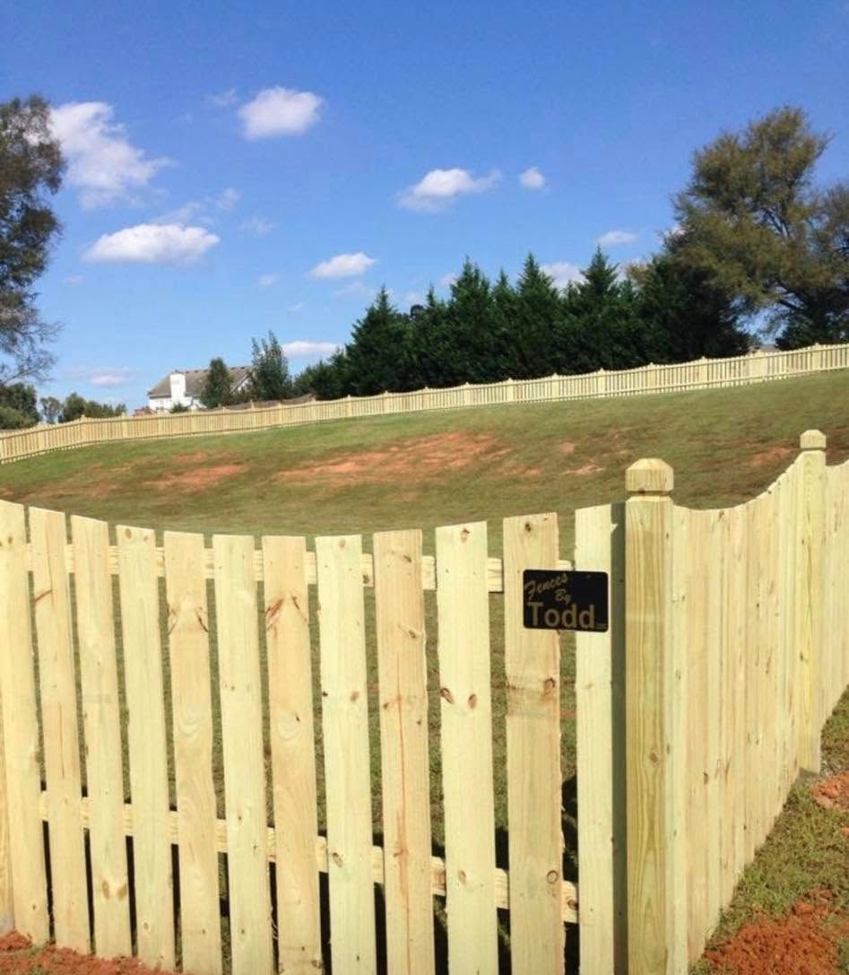 Light wooden fence around a grassy yard under a blue sky, with a small sign on the gate.