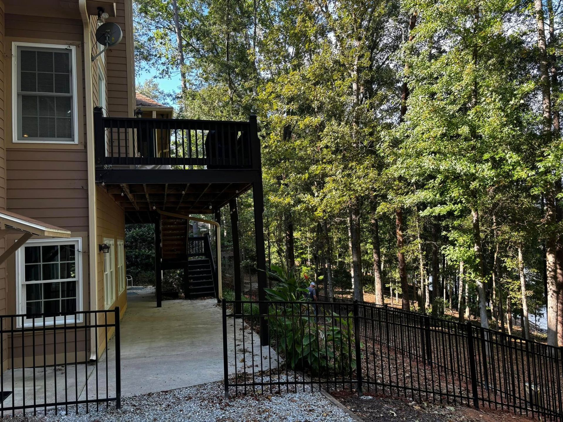 Apartment building balcony and concrete patio beside a black metal fence, with trees in the background