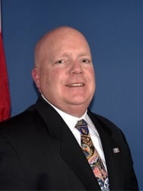 A man in a suit and tie is standing in front of a flag.