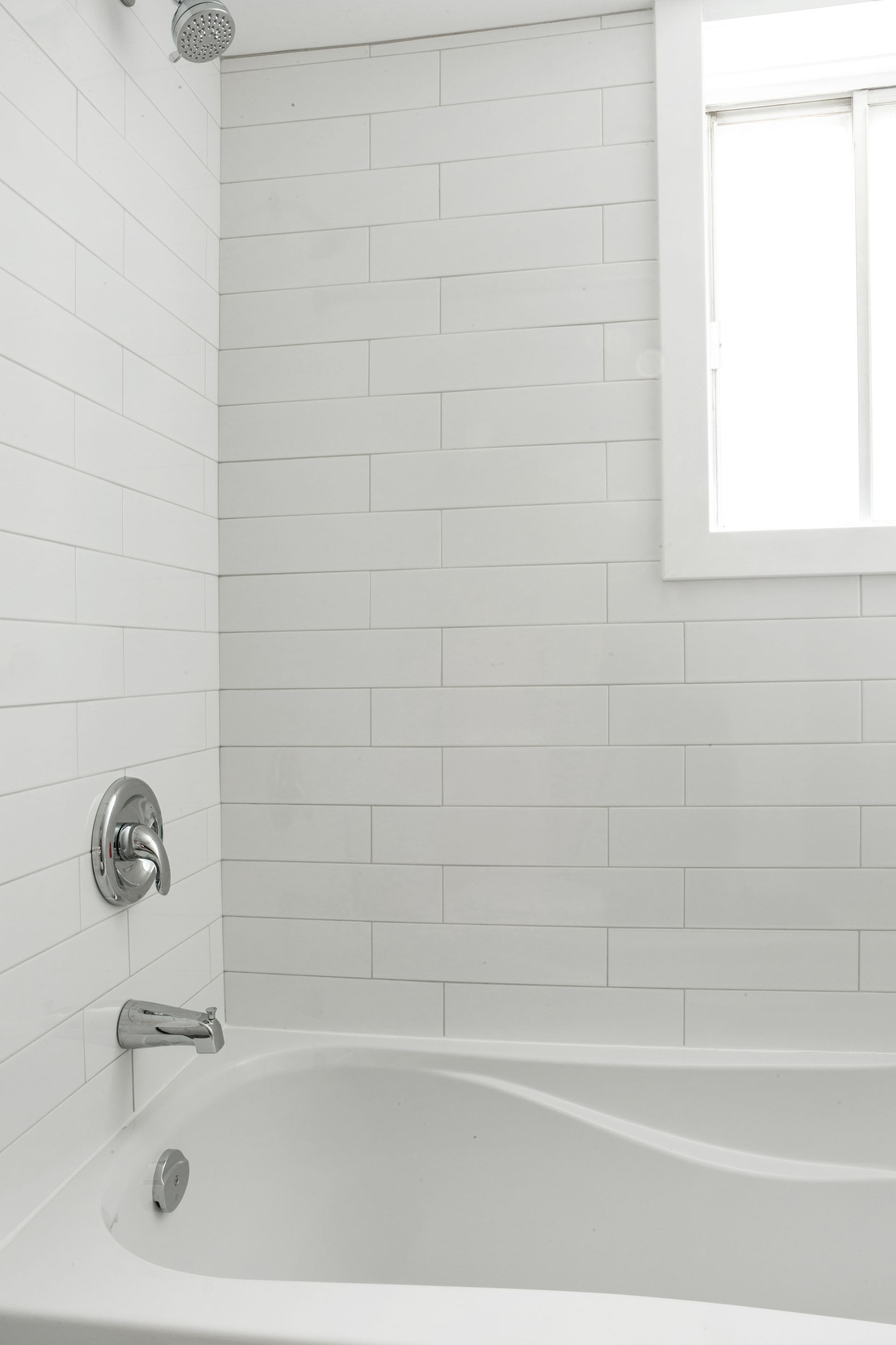 Une baignoire dans une salle de bain avec du carrelage blanc et une fenêtre.