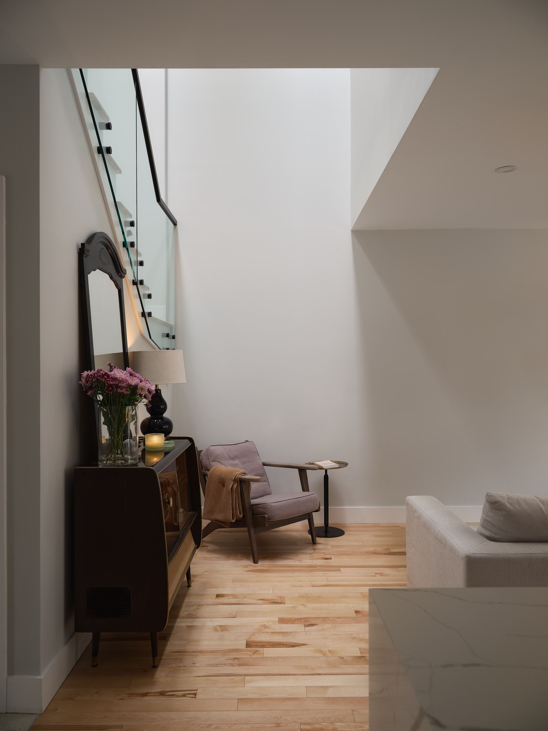 Un couloir étroit avec une chaise, une commode, un miroir et des escaliers.