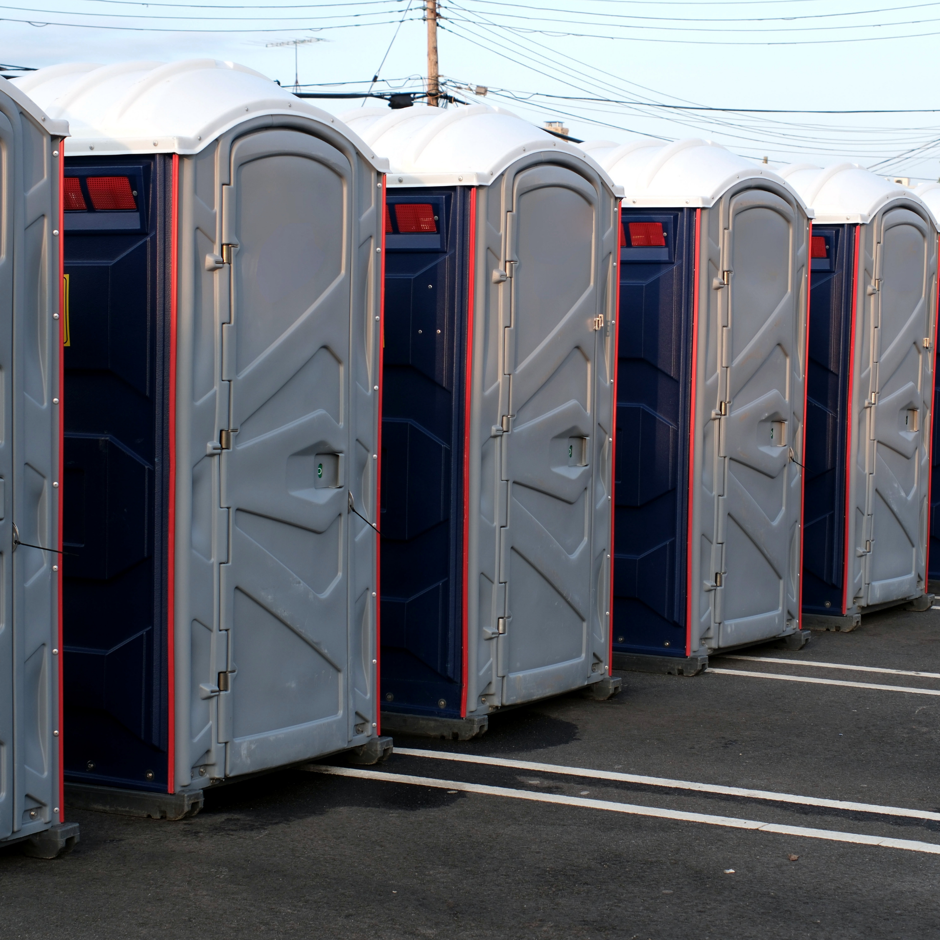 Row of gray portable toilets lined up in a parking lot