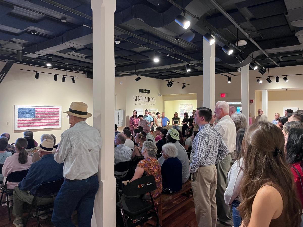 Audience seated in a hall, watching a presentation with an American flag slide on screen.