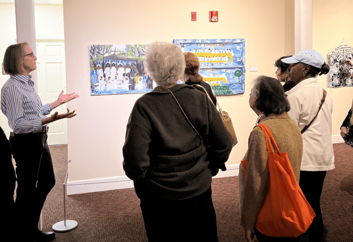 People viewing a wall display in a gallery, with a speaker pointing toward the artwork.