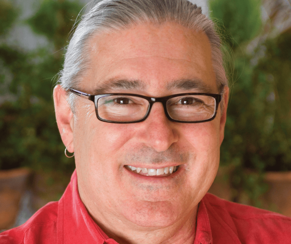 Smiling person wearing glasses and a red shirt, outdoors with a blurred green background