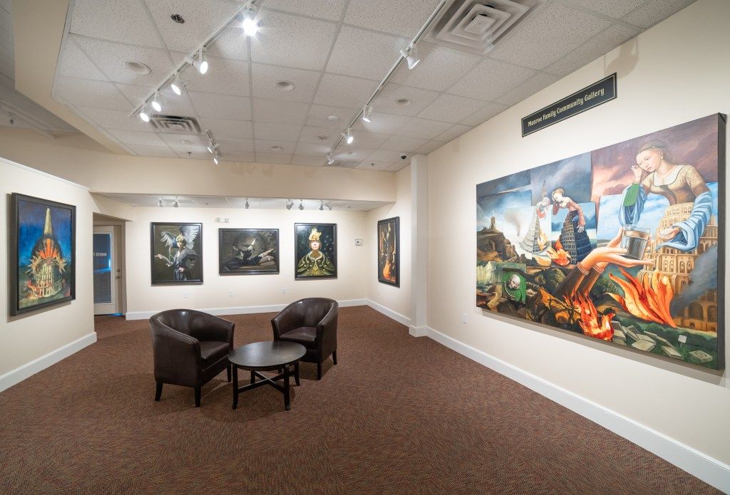 Art gallery with framed paintings, a seating area, and brown carpeted floor.