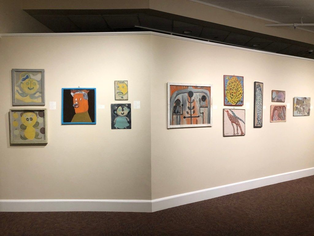 Gallery wall with small colorful paintings displayed along a corner in a white-walled hallway