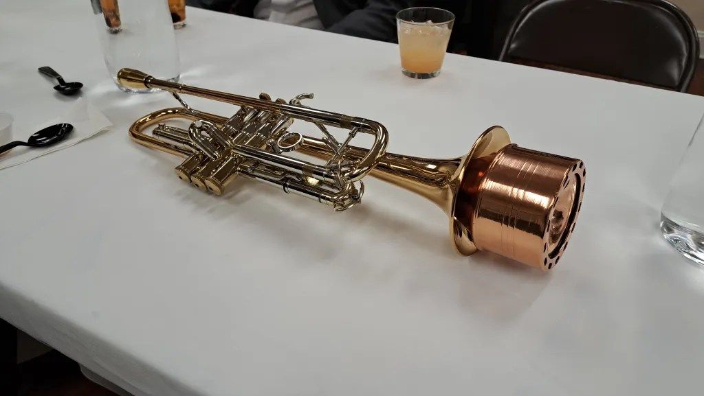 Copper and brass metal sculpture on a white table, with a drink cup in the background.