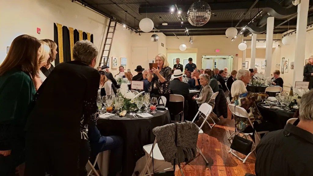 People mingling at a lively indoor event with tables, hanging lights, and a disco ball.