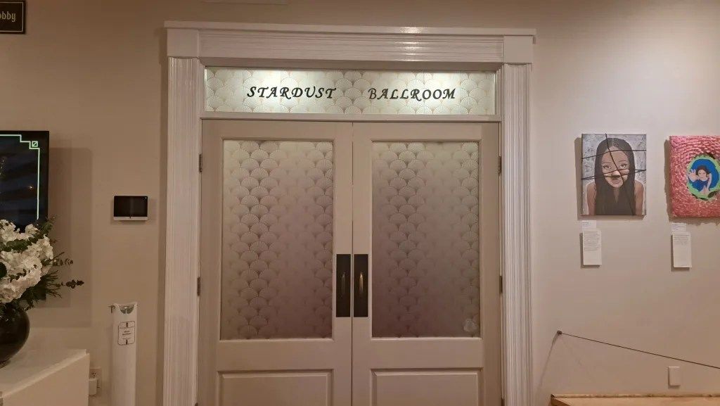 Double wooden doors with frosted glass panels in a beige hallway, flanked by framed artwork.