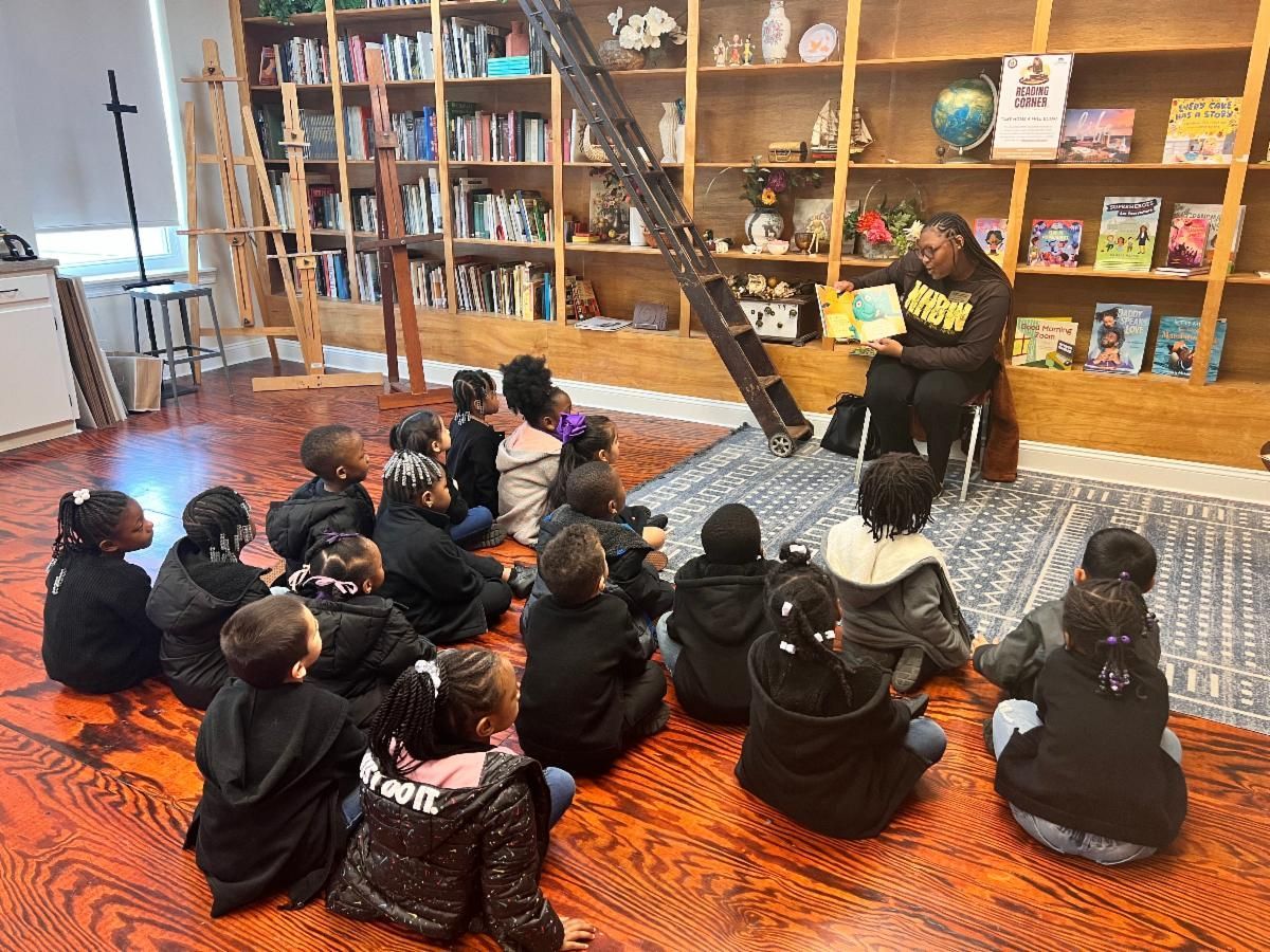 Children sit on a rug listening to a speaker in a bookstore with shelves of books and a ladder behind them.