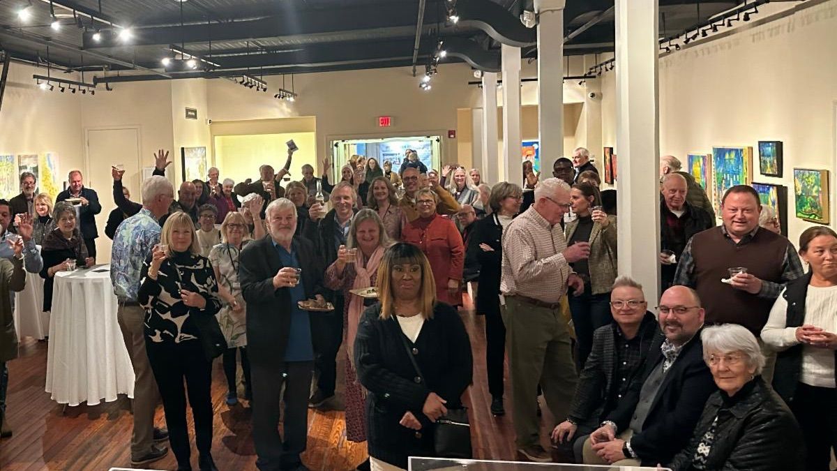 Crowd gathered in an art gallery, posing and mingling under warm lights with colorful paintings on the walls