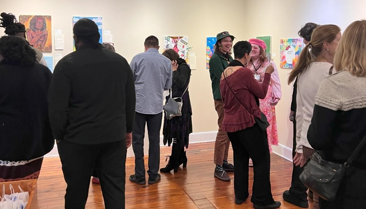 People viewing colorful artwork in a gallery, standing and talking on a wood floor